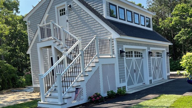 A two-story house with a front porch, a staircase, and a garage. - Cute, cozy and newly built bungalow on private street awaits your Capecod visit. (Mashpee)