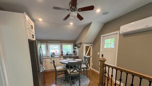 A kitchen with a dining area, wooden flooring, and a ceiling fan. - Cute, cozy and newly built bungalow on private street awaits your Capecod visit. (Mashpee)