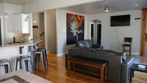 A modern living room with a sofa, a dining area with stools, a kitchen with cabinets, and a painting on the wall. - Sleeps 25 | Theater Room | Near Roaring Springs | Large Meridian Home (Meridian)