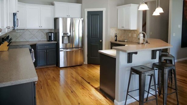 A modern kitchen with stainless steel appliances, a central island, bar stools, and a dark door. - Sleeps 25 | Theater Room | Near Roaring Springs | Large Meridian Home (Meridian)