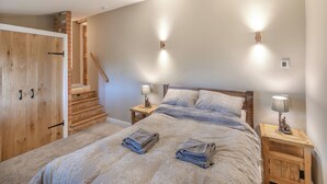 A bedroom with a bed, nightstands, a wooden wardrobe, a staircase, and wall-mounted lights.