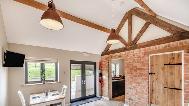 A spacious kitchen with a brick wall, a dining area with a table and chairs, and a living room with a sofa.