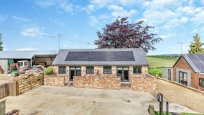 A brick house with solar panels, a garage, and a gravel driveway.