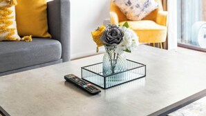A modern living room with a grey sofa, yellow cushions, a glass vase with flowers, and a remote control on a marble coffee table. - STYLISH-BIRMINGHAM central home!!! (Birmingham)