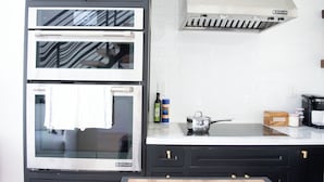 A kitchen with a double oven, a stainless steel range hood, and a countertop with a kettle and a box.
