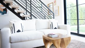 A modern living room with a white sofa, a wooden coffee table, and a staircase with black railings.