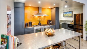 A modern kitchen with a central island, stainless steel appliances, and a bright orange accent wall.