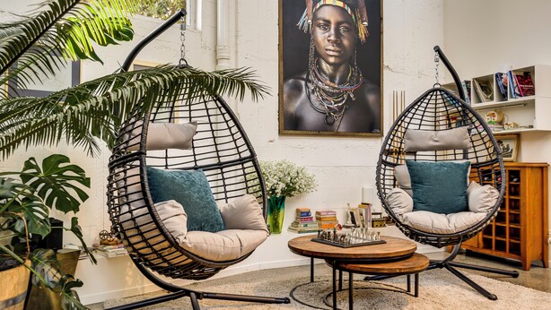 Two hanging chairs with cushions, a round wooden table, and a bookshelf with books and decorative items.