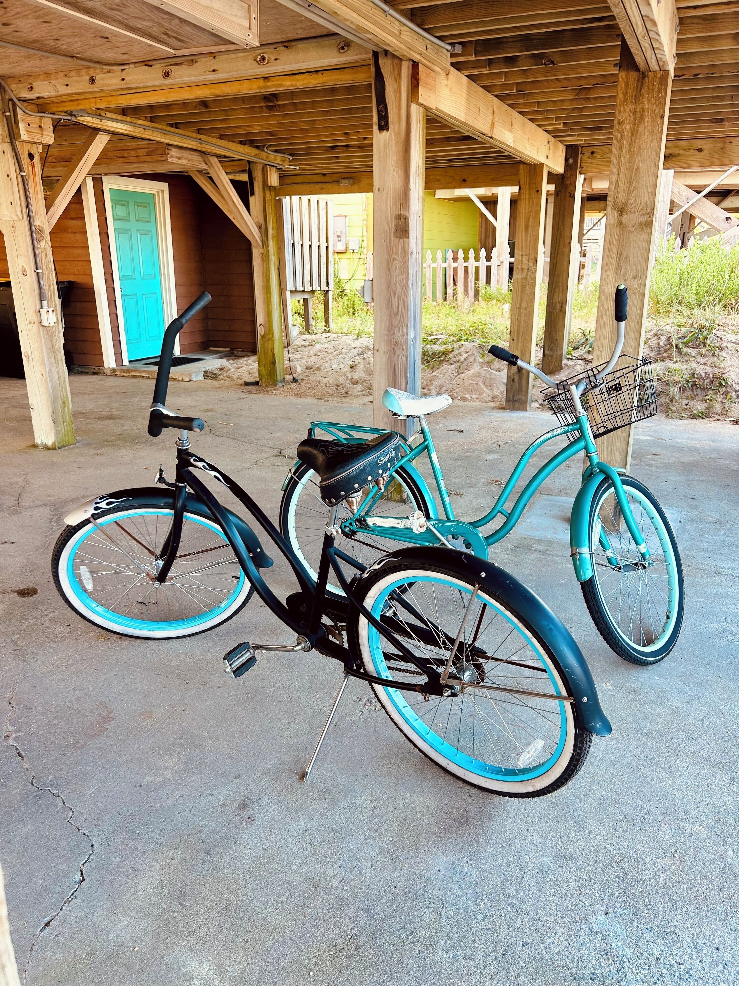 Een overdekt buitengebied met een houten constructie, twee fietsen en een turquoise deur.