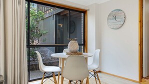 A room with a large window, a round wall clock, a small table with chairs, and a decorative vase. - Coastal Haven in Long Beach (Long Beach)