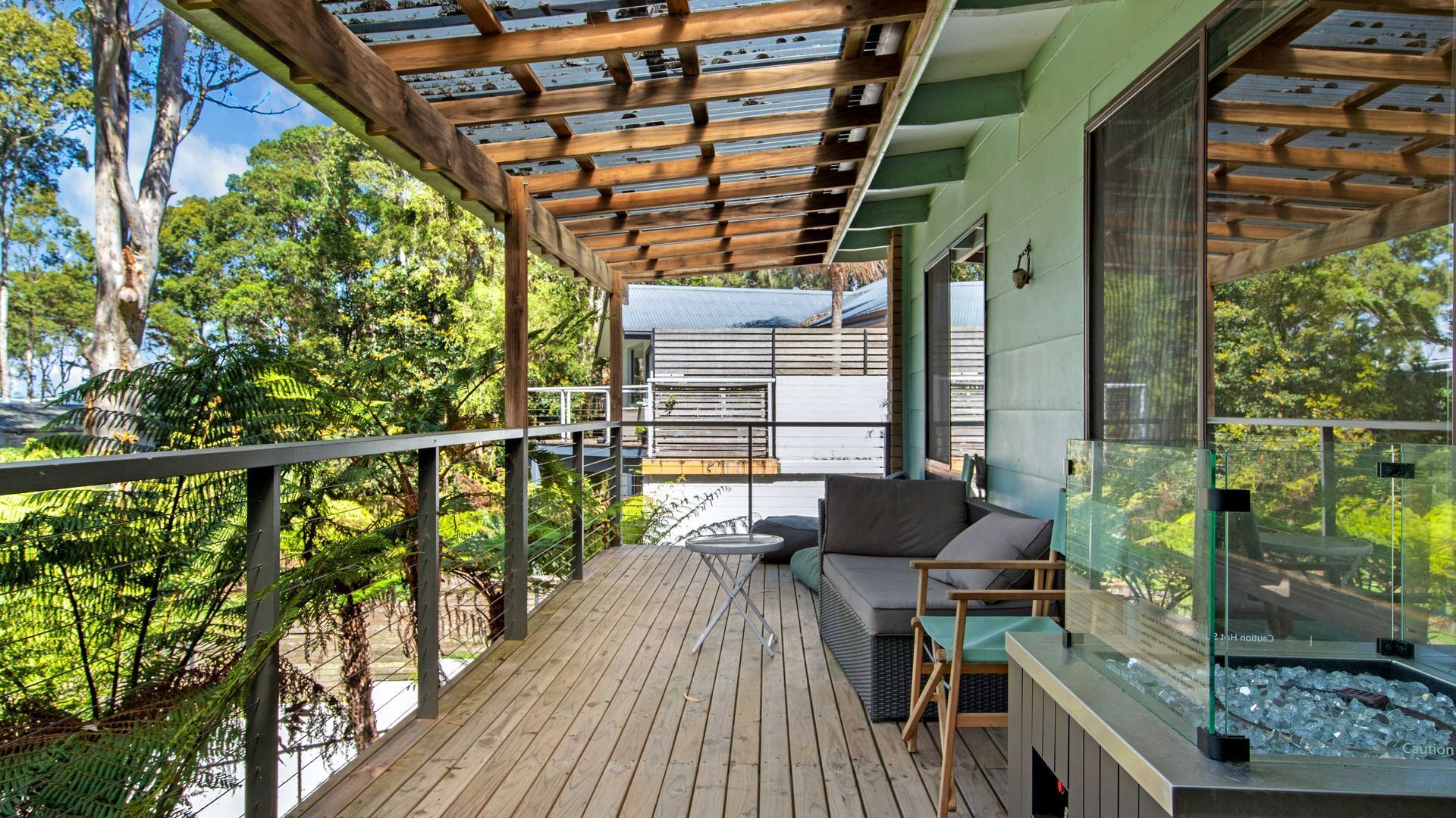 Eine Holzdachterrasse mit Glasverkleidung, einer gepolsterten Sitzgelegenheit und Blick ins grüne Umfeld.
