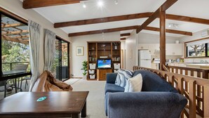 A cozy living area with a sofa, a TV, a wooden bookshelf, and a kitchen visible through an open door. - Coastal Haven in Long Beach (Long Beach)