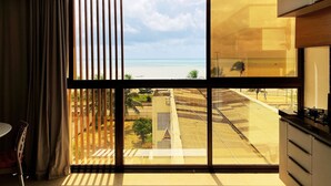 A modern kitchen with a large window overlooking a beach. - Flat FM20 Cabo Branco Lotus - By Almare (João Pessoa)