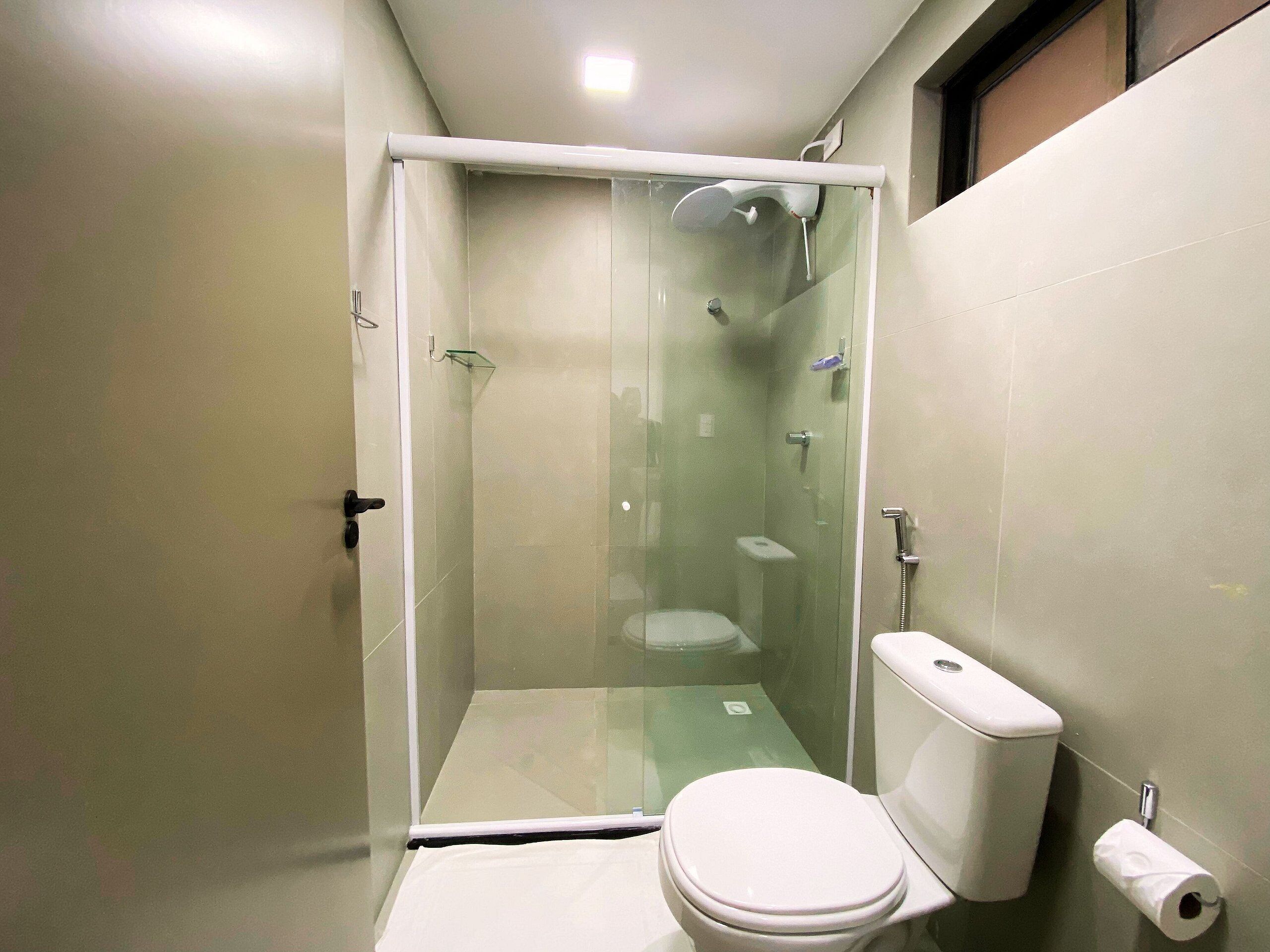 A small, modern bathroom with a glass-enclosed shower, a toilet, and a toilet paper holder.
