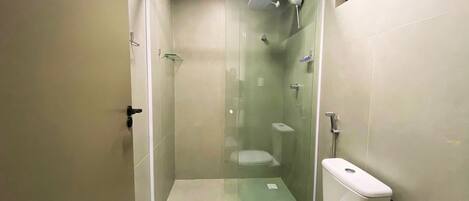 A small, modern bathroom with a glass-enclosed shower, a toilet, and a toilet paper holder.