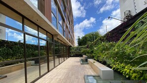 A modern building with large windows, a wooden floor, and a garden area with plants and a water feature. - Flat FM20 Cabo Branco Lotus - By Almare (João Pessoa)