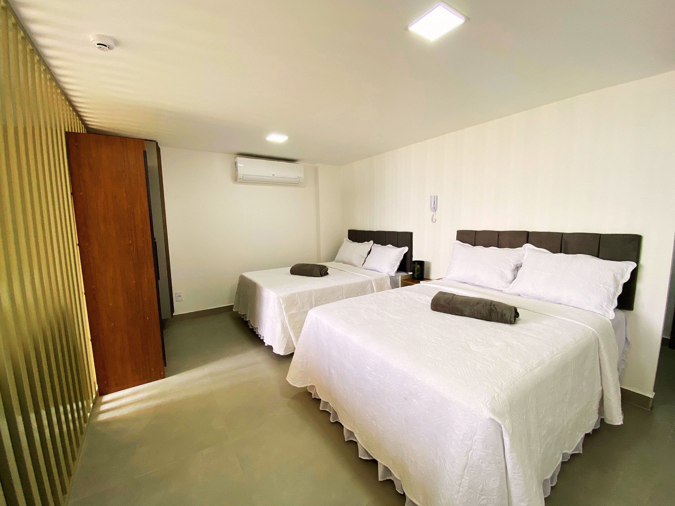 Ein Hotelzimmer mit zwei Einzelbetten, einer Holztür, einer weißen Klimaanlage und einem Telefon an der Wand.