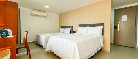 A hotel room with two beds, a wooden door, a chair, an air conditioning unit, and a phone on the wall.