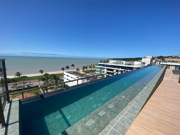 Ein langer Swimmingpool mit klarem Wasser, neben einem modernen Gebäude mit Blick auf Strand und Meer.