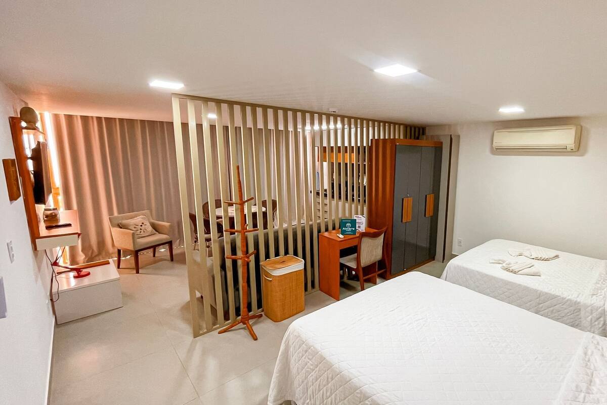 A hotel room with two beds, a desk, a chair, a mirror, and a partition.