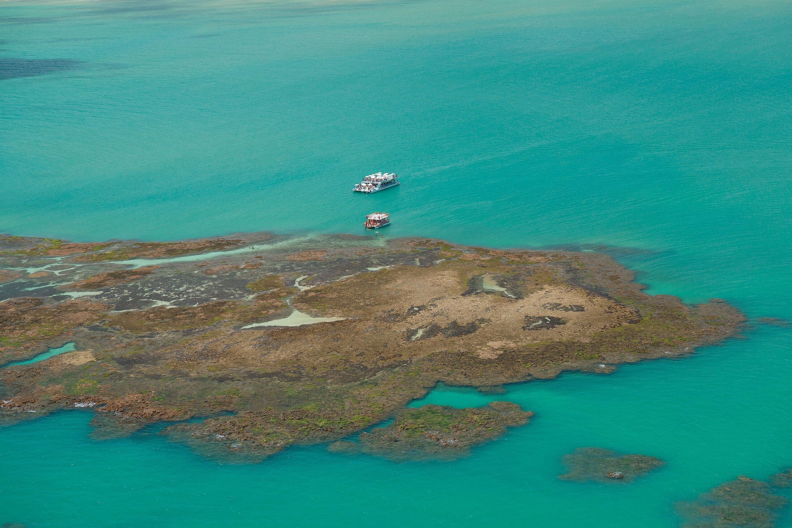 An aerial view of a coastal area with two boats and a rocky shoreline.