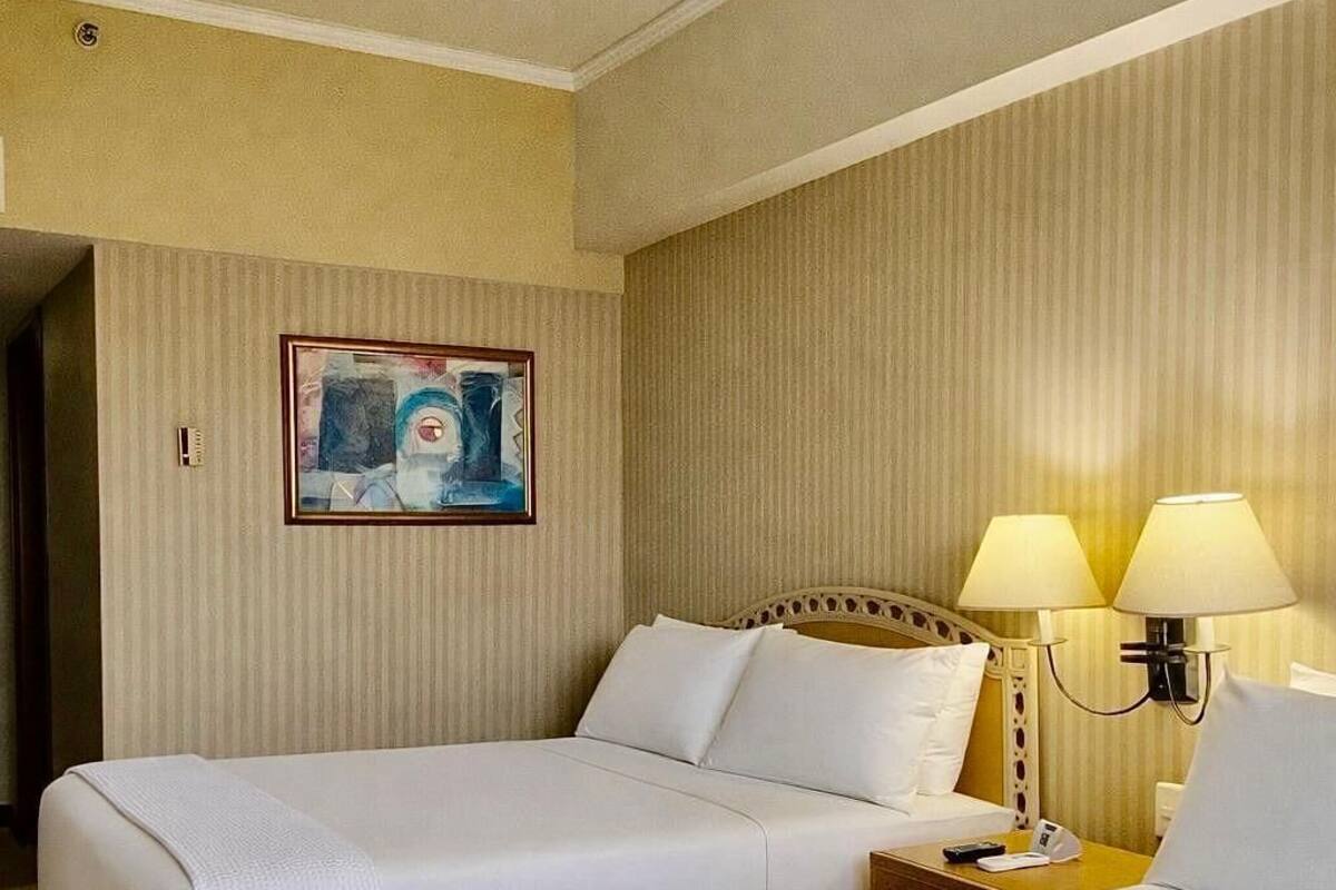 A hotel room with two beds, a painting on the wall, and two bedside lamps.