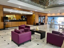 Un hall con sofás morados, un mostrador de recepción y vistas al exterior.