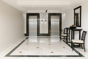 A hallway with two elevators, a polished marble floor, and a small table with chairs. - Intercity Tower Hotels  (San Pedro Sula)