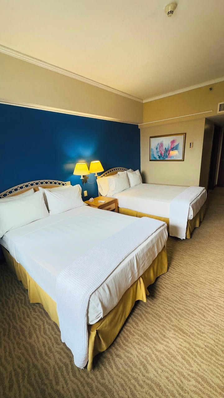 A hotel room with two beds, a painting on the wall, and a carpeted floor.