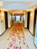 Un pasillo de hotel con alfombra estampada, puertas y luces fijadas a la pared.
