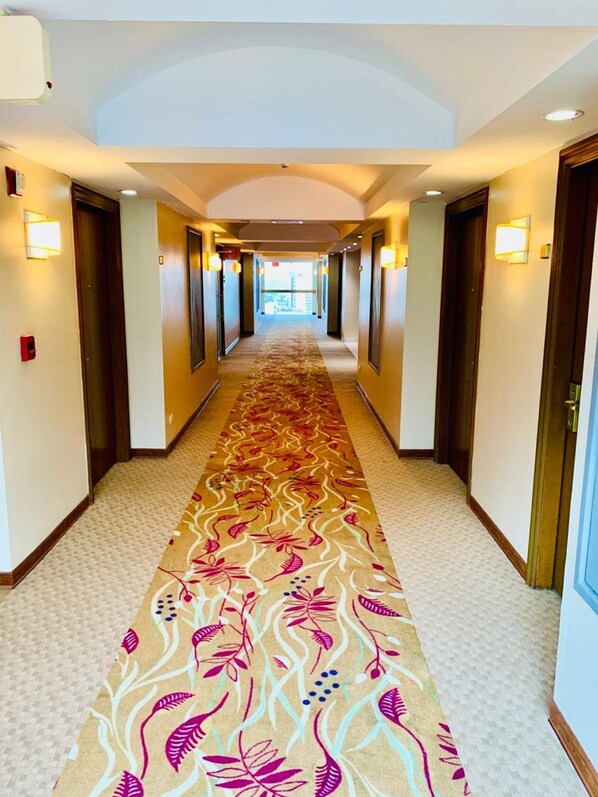 A hotel hallway with a patterned carpet, doors, and wall-mounted lights. - Intercity Tower Hotels (San Pedro Sula)