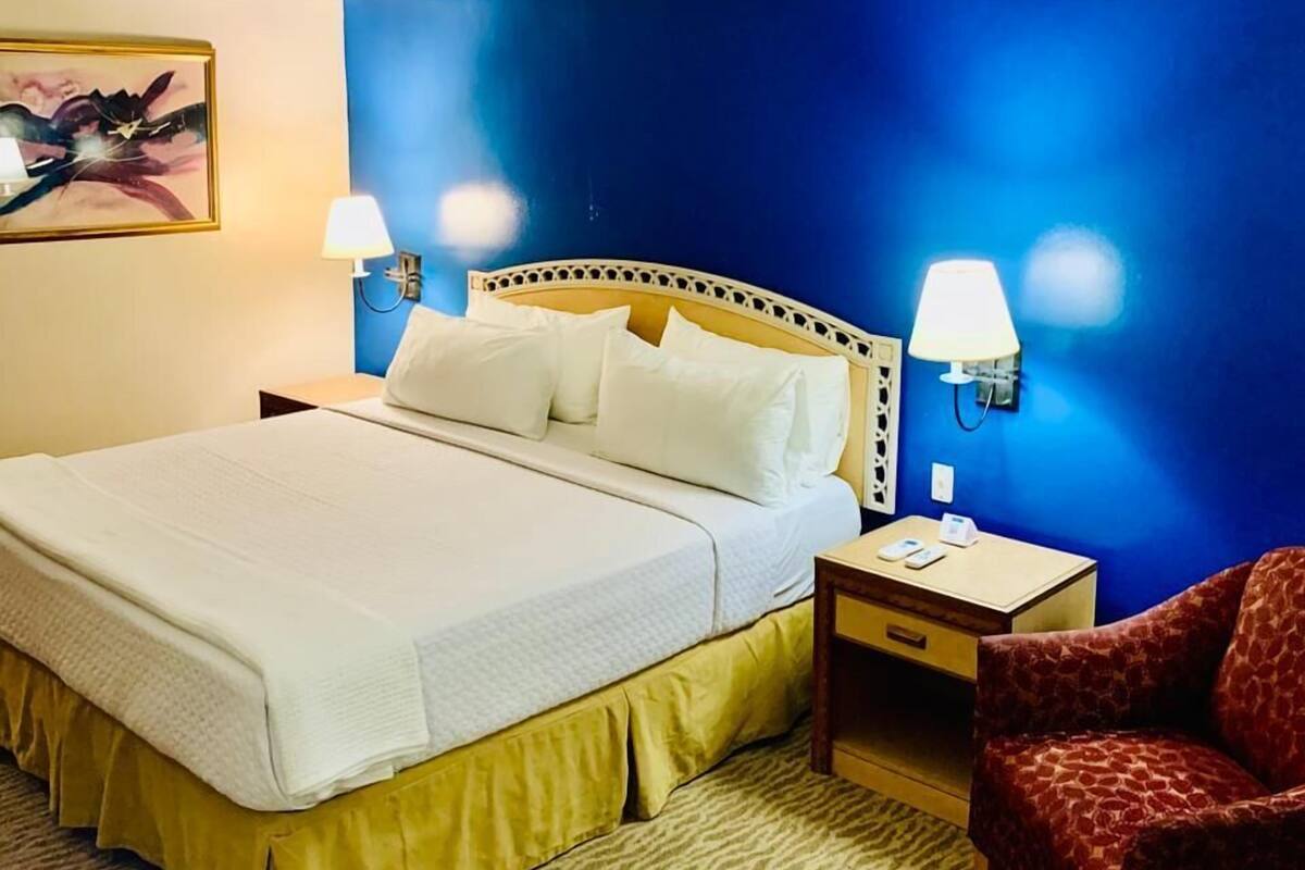 A hotel room with a bed, two bedside lamps, a nightstand, a chair, and a wall-mounted artwork.
