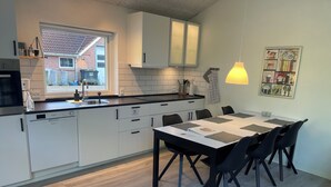 A modern kitchen with white cabinets, a black countertop, and a dining area with a table and chairs. - EMDA country living close to Legoland. (Billund)