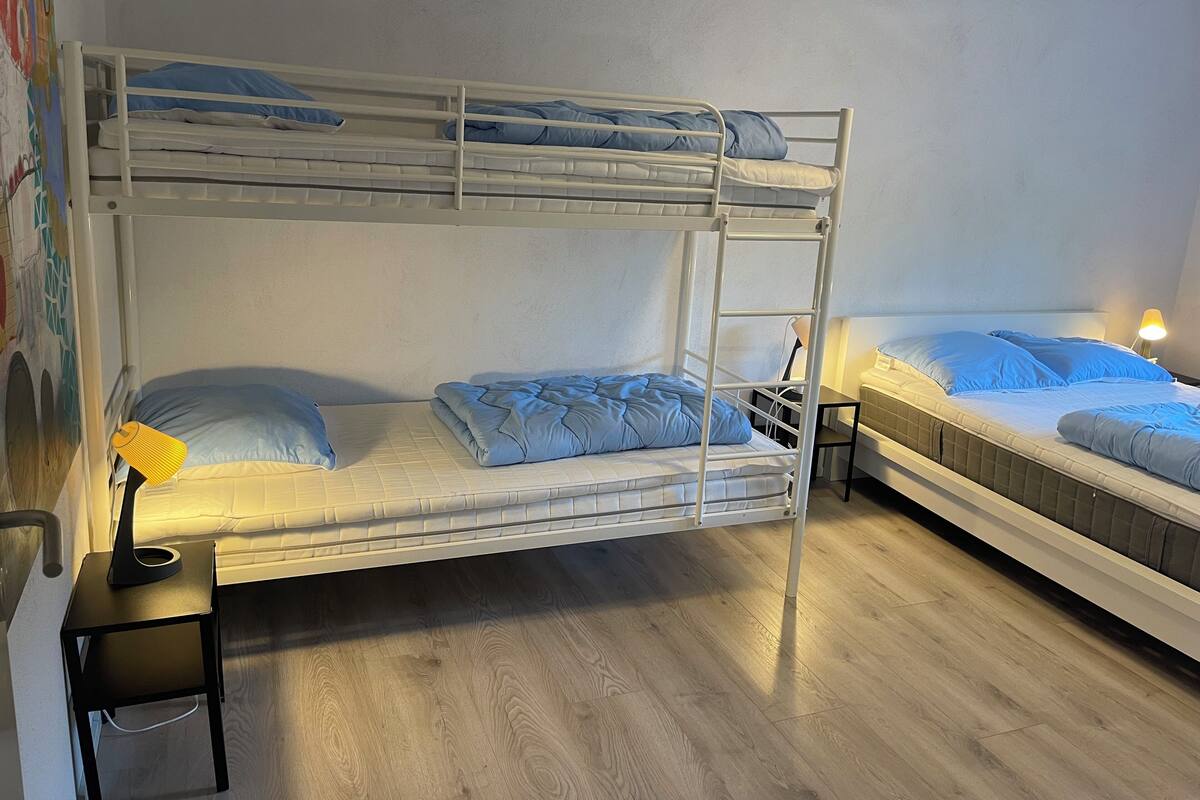 Quarto com beliche, escrivaninha e cadeira, luminária e parede com pintura colorida.