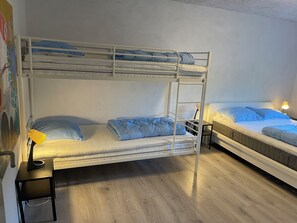 A bunk bed room with a desk and chair, a lamp, and a wall with a colorful painting.