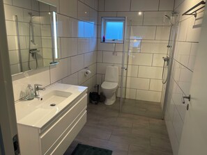 A modern bathroom with a large mirror, a bathtub, a toilet, and a shower area.