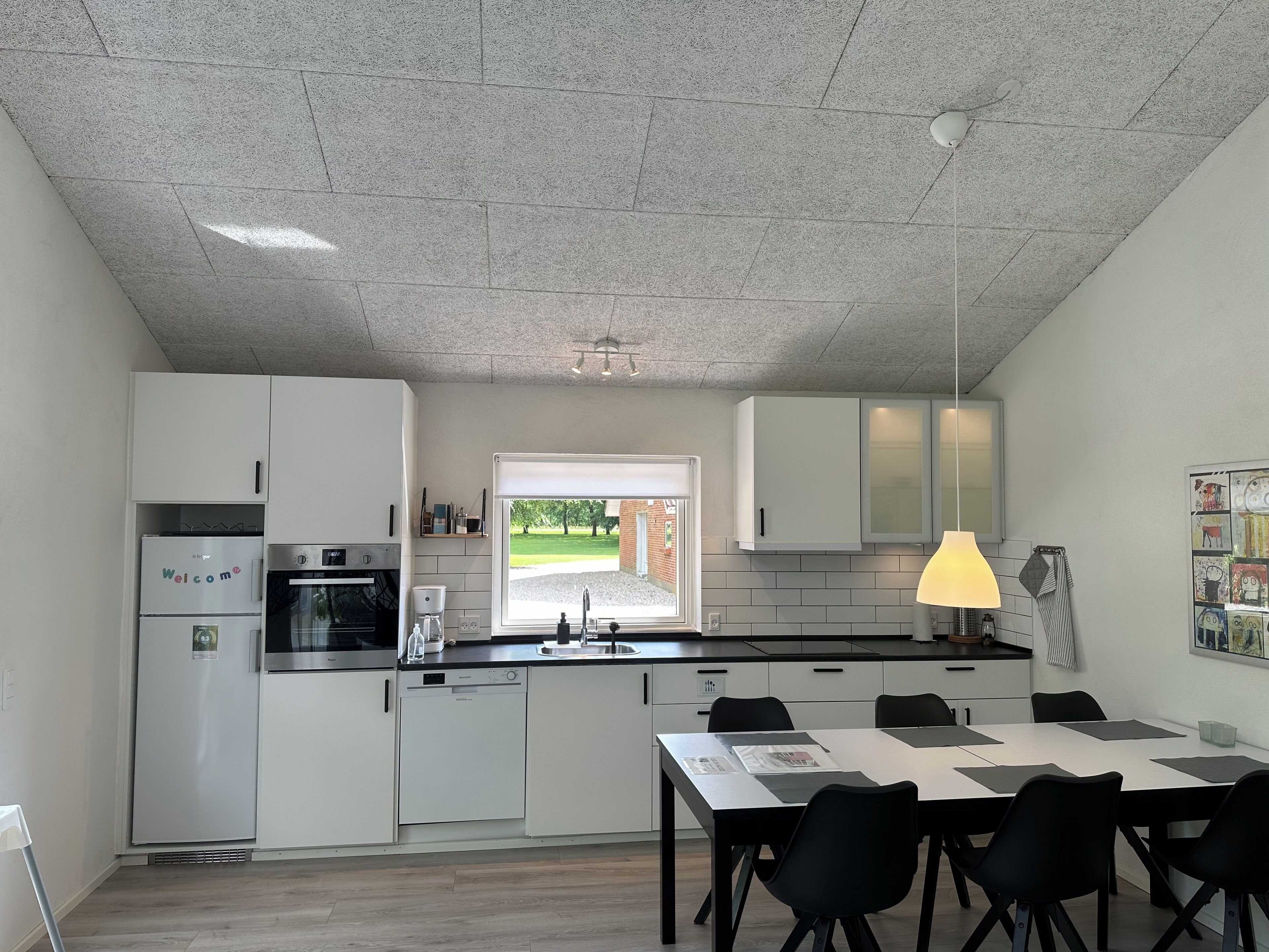 Una cocina moderna con armarios blancos, horno empotrado, lavavajillas y ventana con vistas a un paisaje verde.