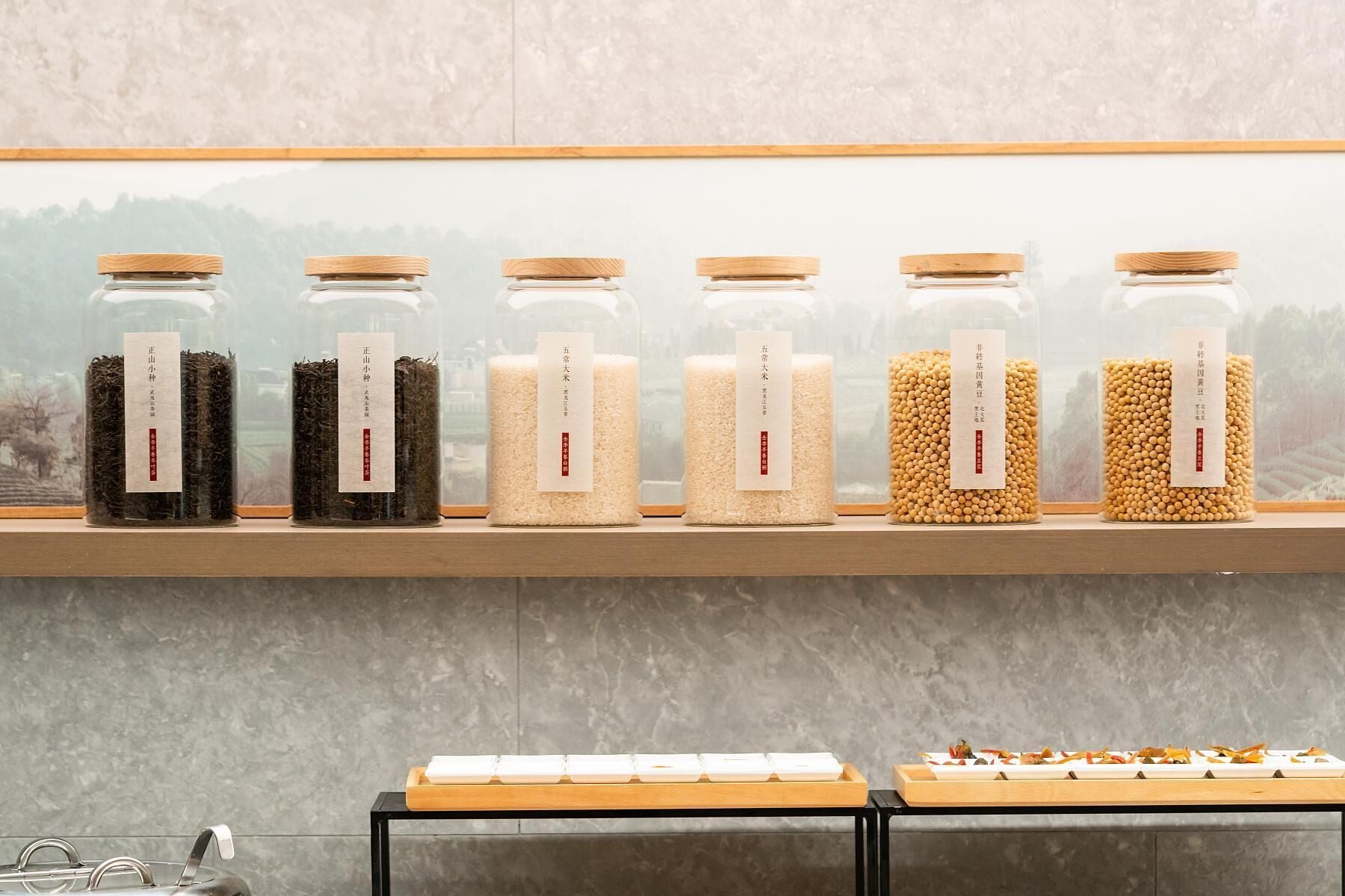 A shelf with six glass jars containing different grains and seeds, each labeled with text.