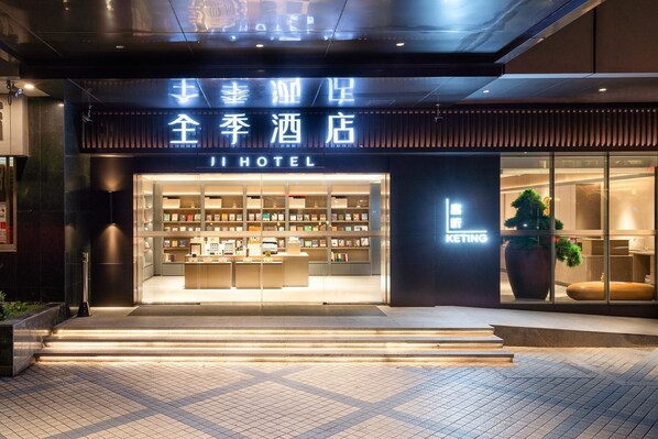 A hotel entrance with a modern design, featuring a glass facade and a well-lit interior displaying books and amenities. - Moon Bay (Guangzhou)