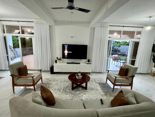 Una sala de estar moderna con un sofá, dos sillones, una mesa de centro y un televisor de pantalla plana sobre un mueble blanco.