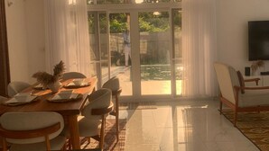 Ein geräumiges Wohnzimmer mit Essbereich, Deckenventilator, Flachbildfernseher und Blick auf einen Swimmingpool durch große Glasüren.