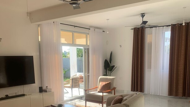 Ein modernes Wohnzimmer mit einer großen Eckcouch, einem Flachbildfernseher und einem Deckenventilator.