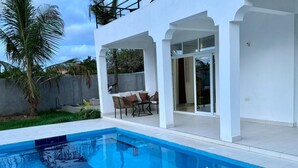 Ein Swimmingpool mit weißer Außenverkleidung und Glastüren, die auf eine überdachte Terrasse führen.