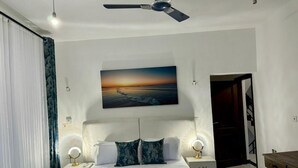 Ein Schlafzimmer mit einem Bett, zwei Nachttischen, einem Deckenventilator, einem Gemälde und einer Tür.