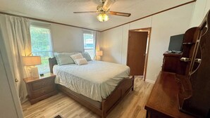 A bedroom with a bed, a wooden dresser, a ceiling fan, and a window with curtains. - Home in Surf City- Pelicans Perch (Hampstead)