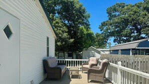 A covered deck with wicker furniture and a white railing. - Home in Surf City- Pelicans Perch (Hampstead)
