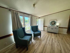 Una habitación con dos sillones tapizados, una consola blanca con un plato decorativo, y una puerta que da al exterior.