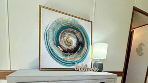 A white wooden console table with a framed abstract painting above it and a "Welcome" sign below. - Home in Surf City- Pelicans Perch (Hampstead)