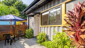 Ein modernes Gebäude mit großem Fenster, einer Terrasse mit Stühlen und Sonnenschirm sowie verschiedenen Pflanzen.