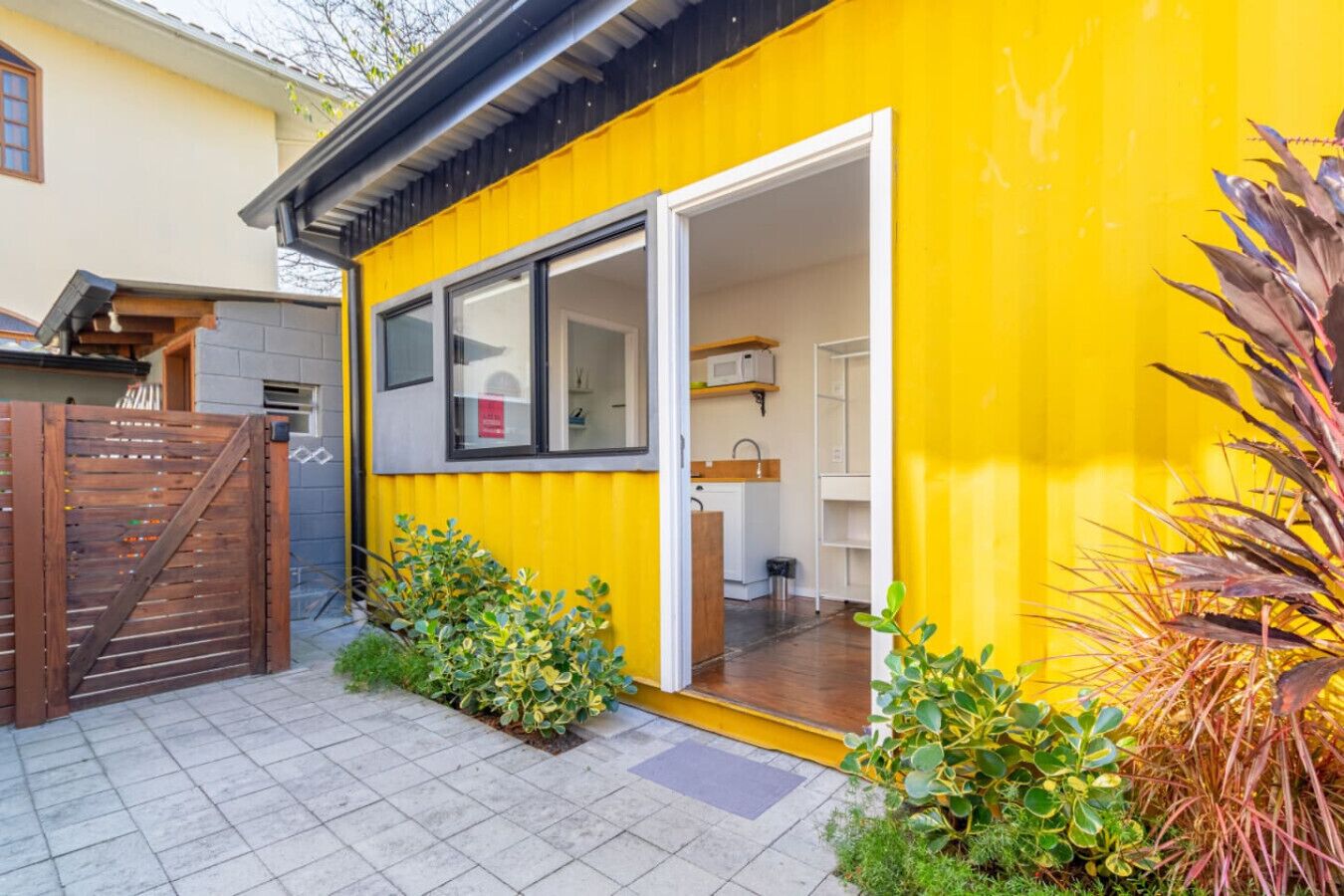 A yellow building with a sliding glass door entrance, a small outdoor kitchen, and a wooden gate.